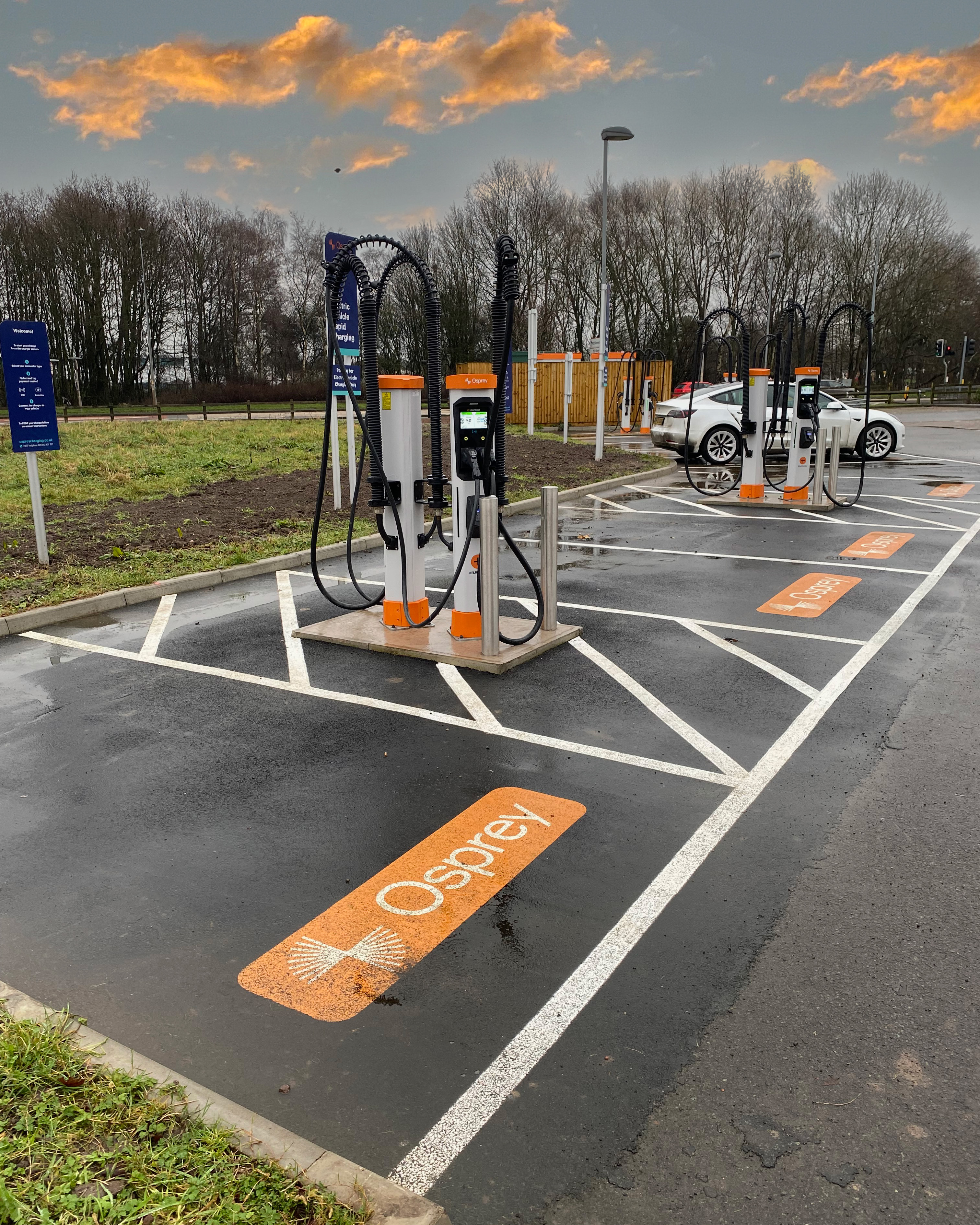 A white electric car charging at a high powered EV charging hub.