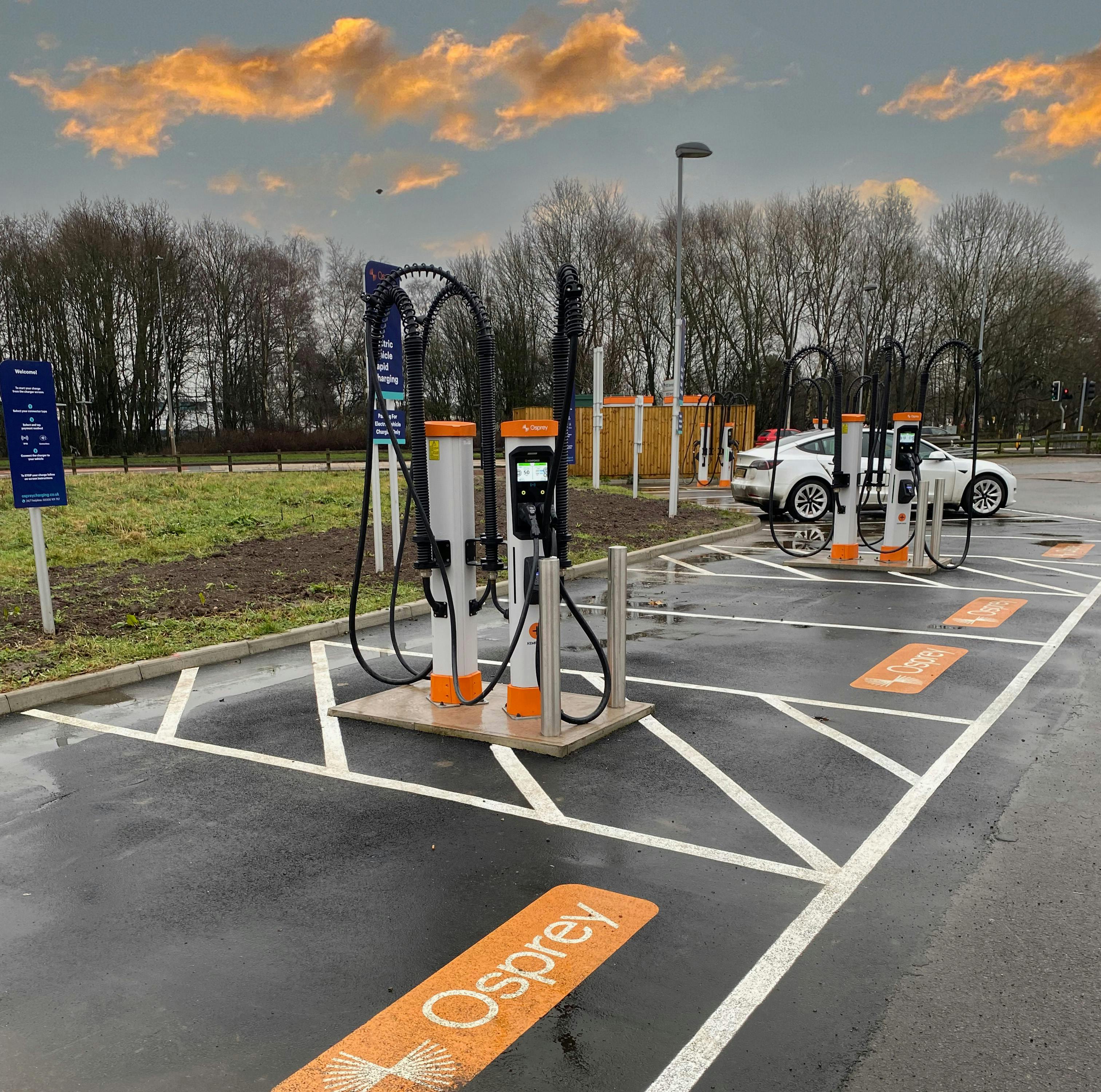 A white electric car charging at a high powered EV charging hub.