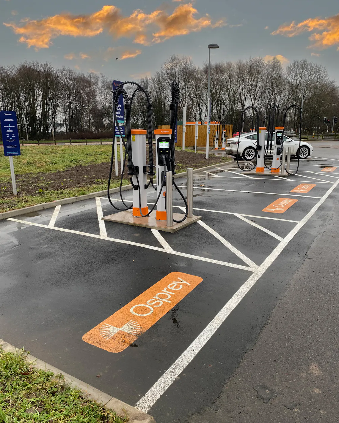 A white electric car charging at a high powered EV charging hub.