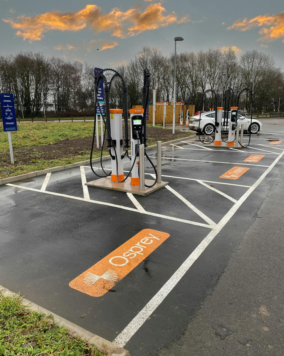 A white electric car charging at a high powered EV charging hub.