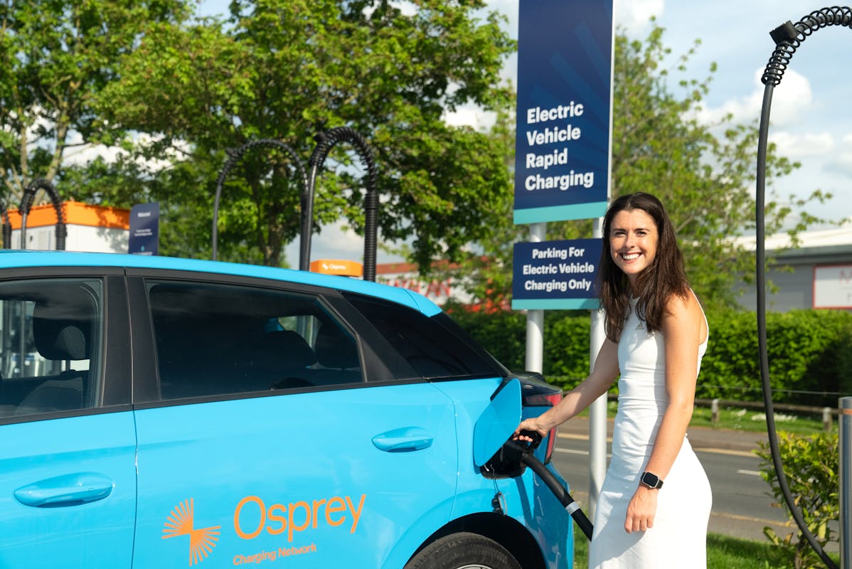 Olivia Breen poses charging a blue electric car at an Osprey rapid charging point. 