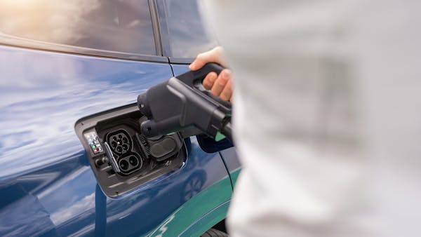 A hand plugging a CCS rapid charging cable into a dark blue electric vehicle