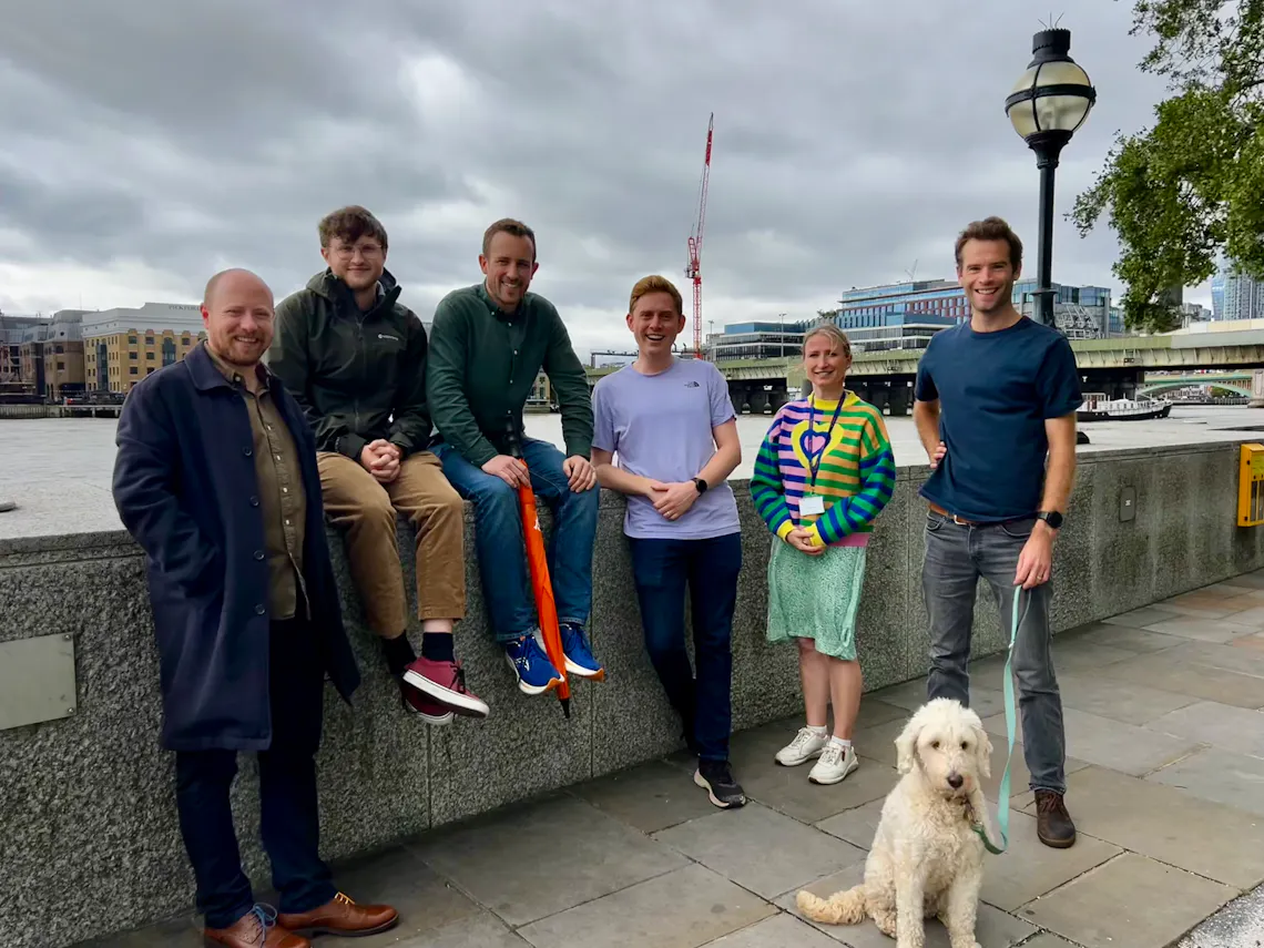 A group of people and a dog pose for a photo in front of the Thames