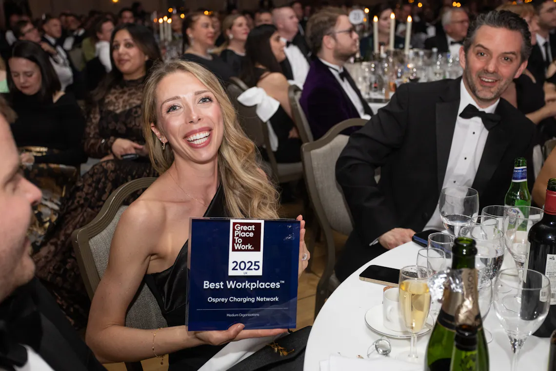 A blonde woman seated at a table holds up an award plaque