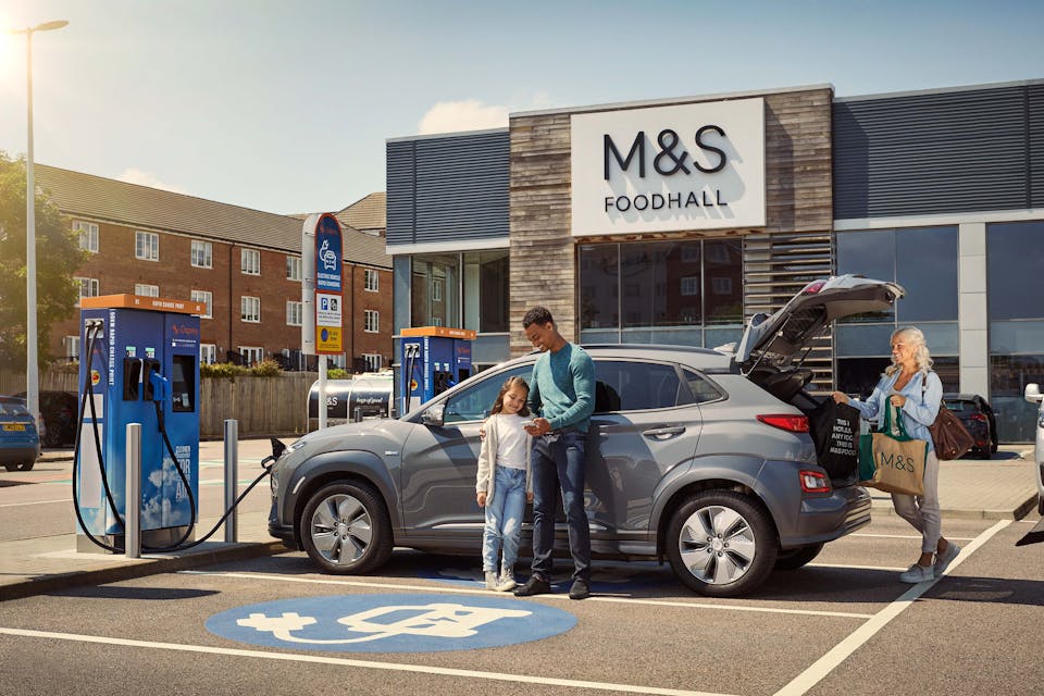 Family returning from M&S food shopping to their charged car at Tonbridge.