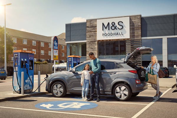 Family returning from M&S food shopping to their charged car at Tonbridge.
