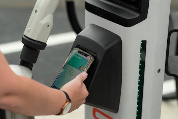 A hand holding an iPhone with Apple Pay open on top of a contactless payment terminal on a rapid charging station.