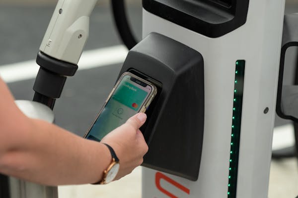 A hand holding a smartphone with Apple Pay active on to the contactless payment terminal on a rapid charger.