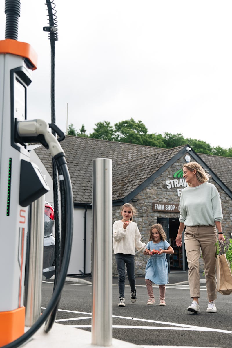 A woman with her two children walking out of a coffee shop towards the Osprey EV rapid charging stations.