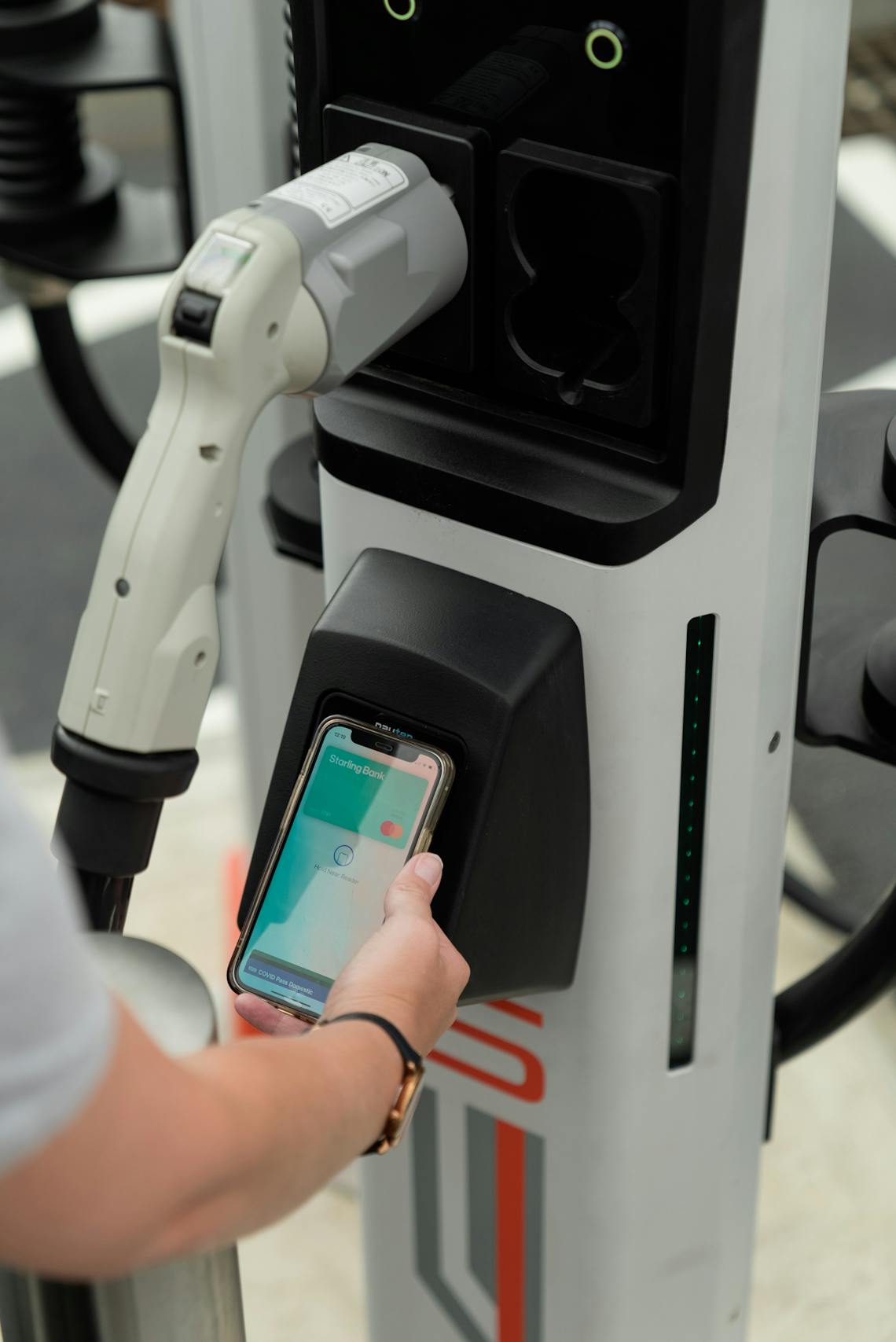 A hand holds a smart phone with Apple Pay open onto the contactless payment terminal of a rapid charger
