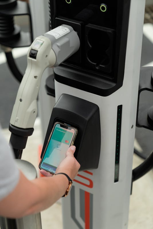 A hand holds a smart phone with Apple Pay open onto the contactless payment terminal of a rapid charger