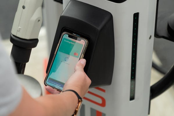 A hand holds a smart phone with Apple Pay open onto the contactless payment terminal of a rapid charger