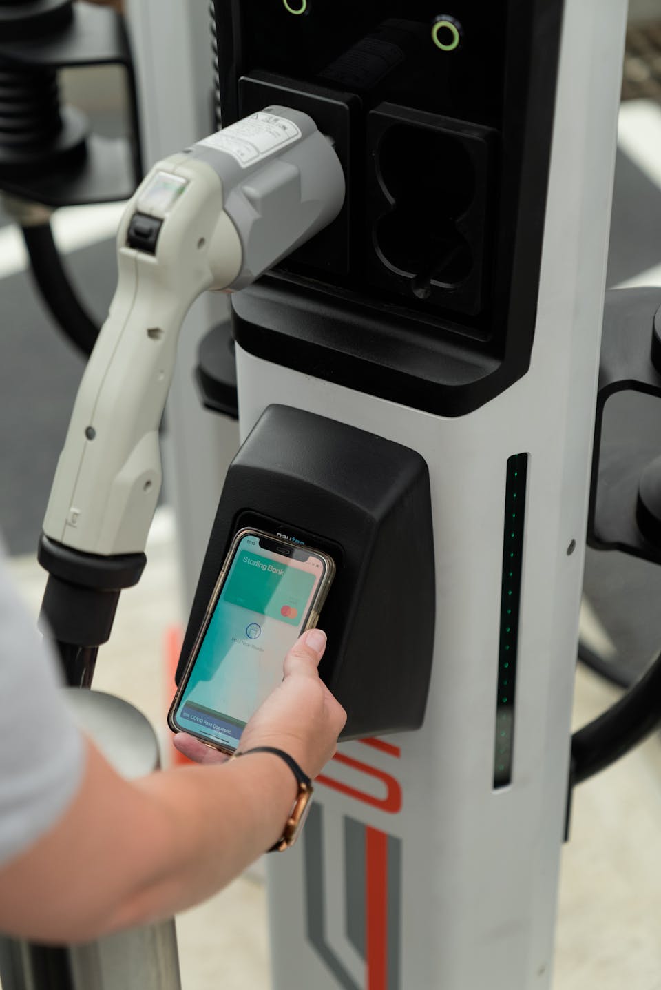 A hand holds a smart phone with Apple Pay open onto the contactless payment terminal of a rapid charger