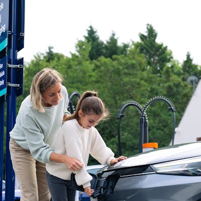 A mother and her child together plugging in the Osprey EV rapid charger into their electric car.