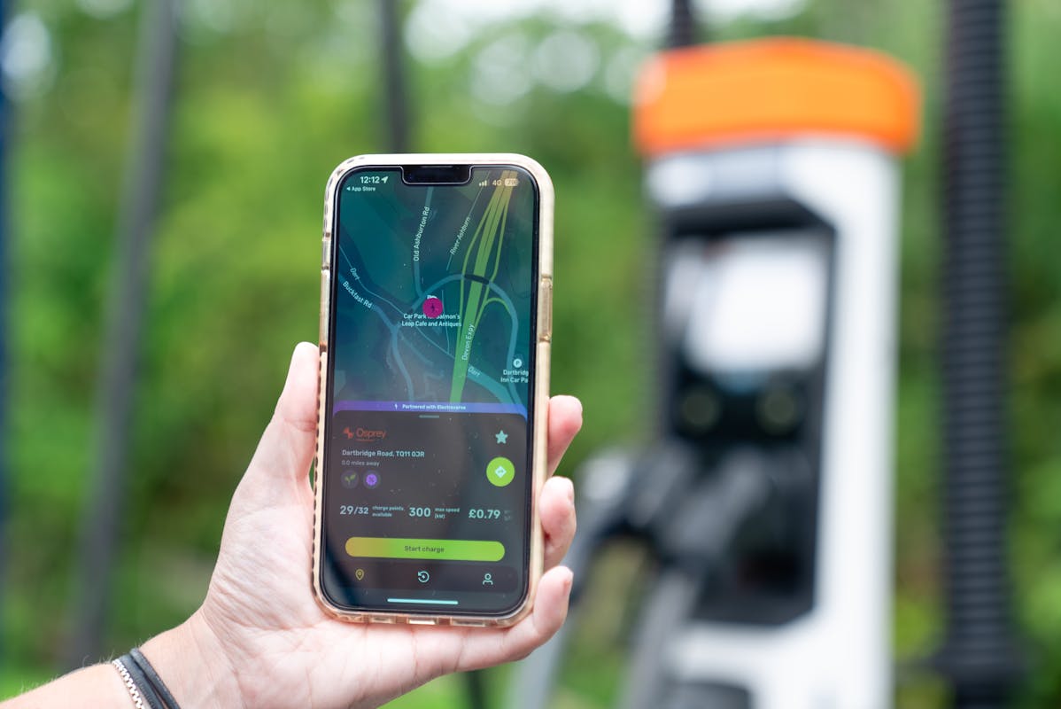 Person holding their phone with Electric Universe app open in front of an Osprey EV rapid charger.