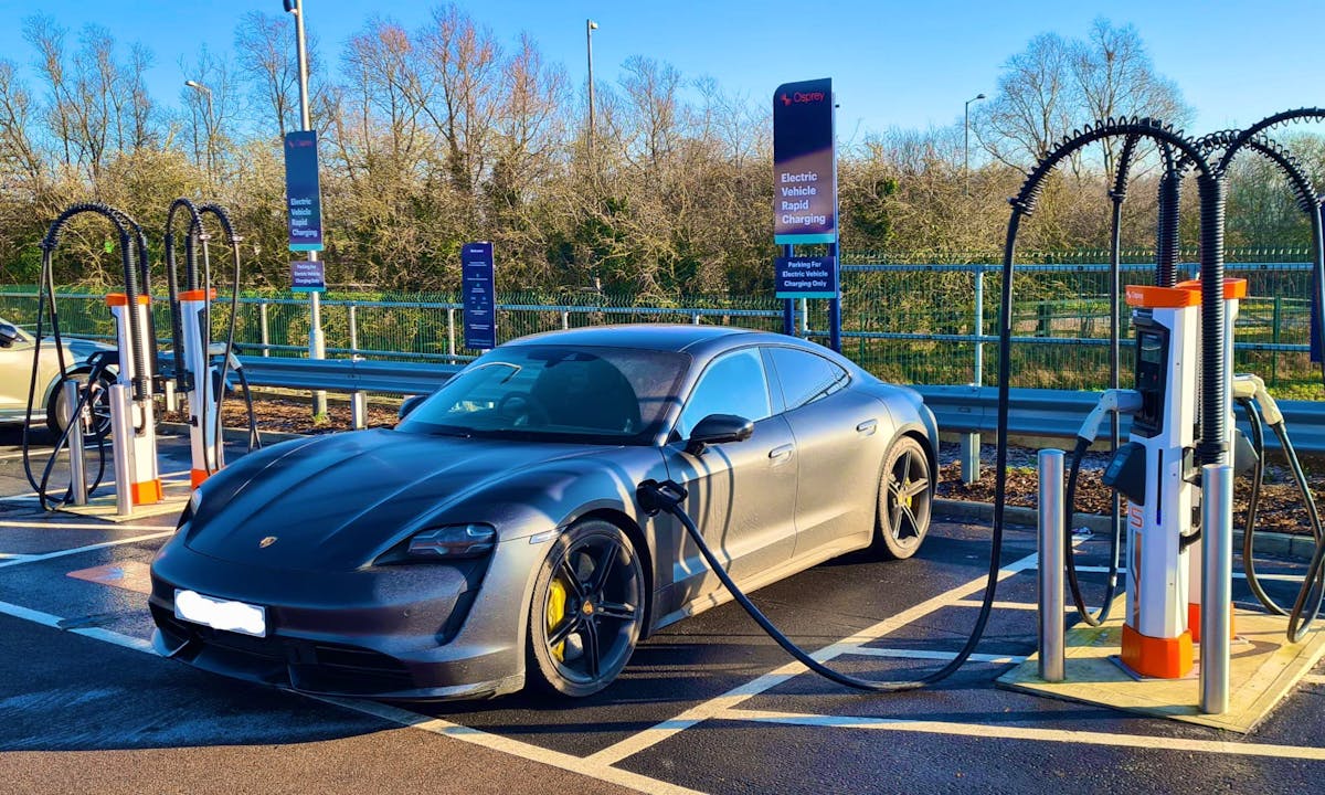 A Porsche Taycan plugged into a 150kW EV charging station at a rapid charging hub.