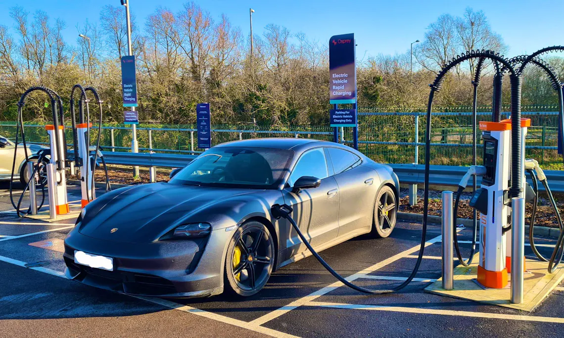 A Porsche Taycan plugged into a 150kW EV charging station at a rapid charging hub.