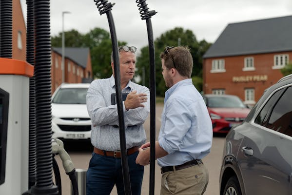 Two men talk together next to an ultra-rapid charging point, with a pub restaurant visible behind