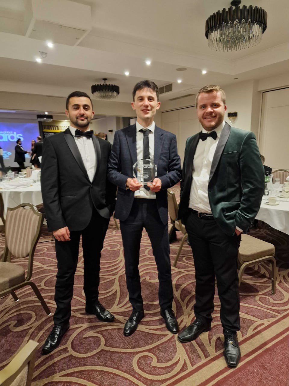 3 men in suits pose for a photo holding an award