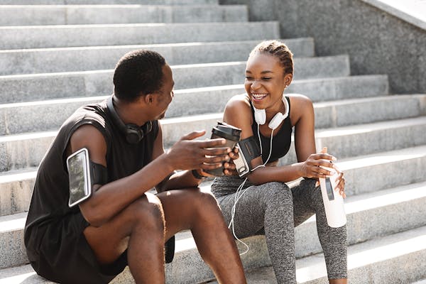 A man and woman in exercise clothing sit on steps drinking and chatting