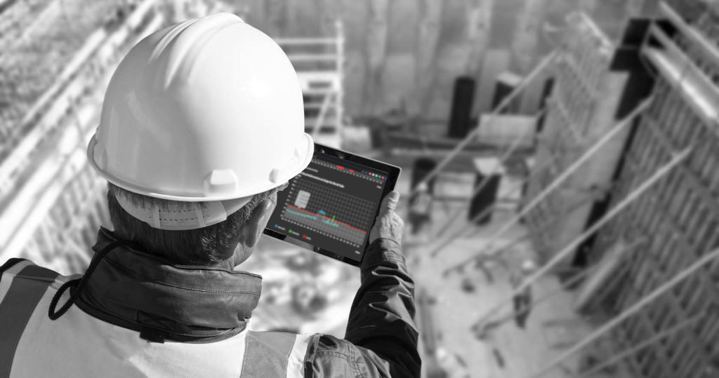 Ingeniero con casco blanco y chaleco de seguridad utilizando una tablet con la plataforma de OTOH abierta para seguir en tiempo real los niveles de ruido en una obra de construcción. La plataforma OTOH muestra gráficos de intensidad sonora y alertas de picos de ruido.