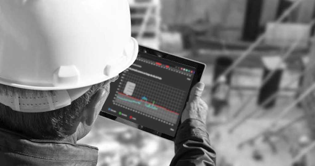Engenheiro de capacete branco e colete de segurança usando um tablet com a plataforma da OTOH aberta para acompanhar em tempo real os níveis de ruído em uma obra de construção civil. A plataforma OTOH exibe gráficos de intensidade sonora e alertas de picos de ruído.