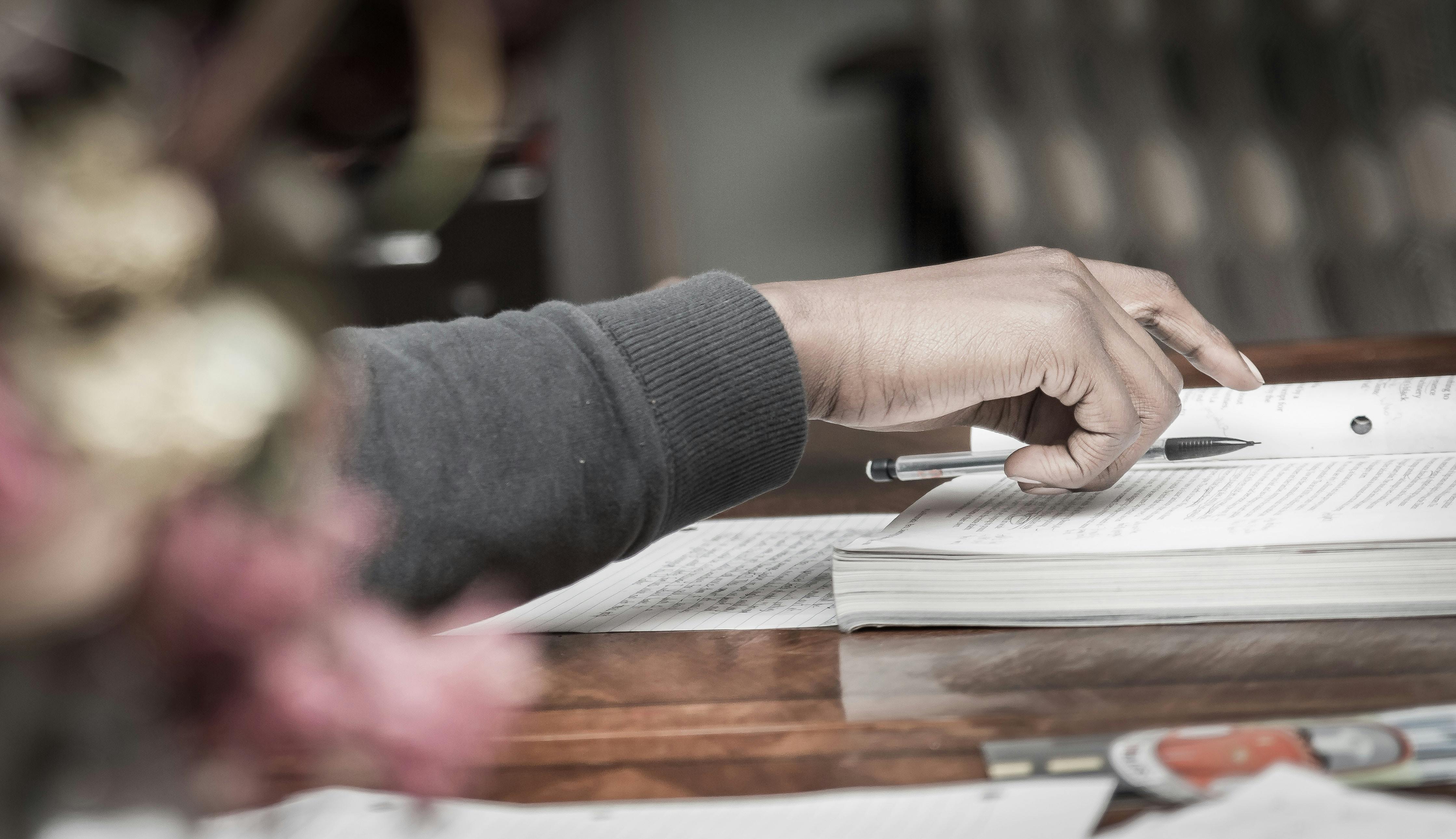 Student pictured holding pen, taking notes while reading text book