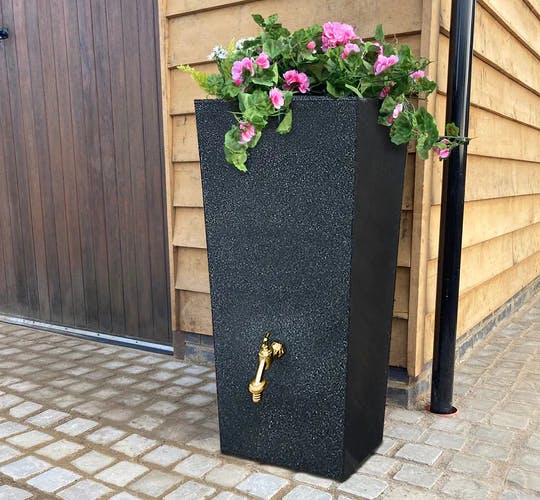 A photograph of a rain planter - a water tank with a space on top for planting flowers, and a bronze tap on the front.