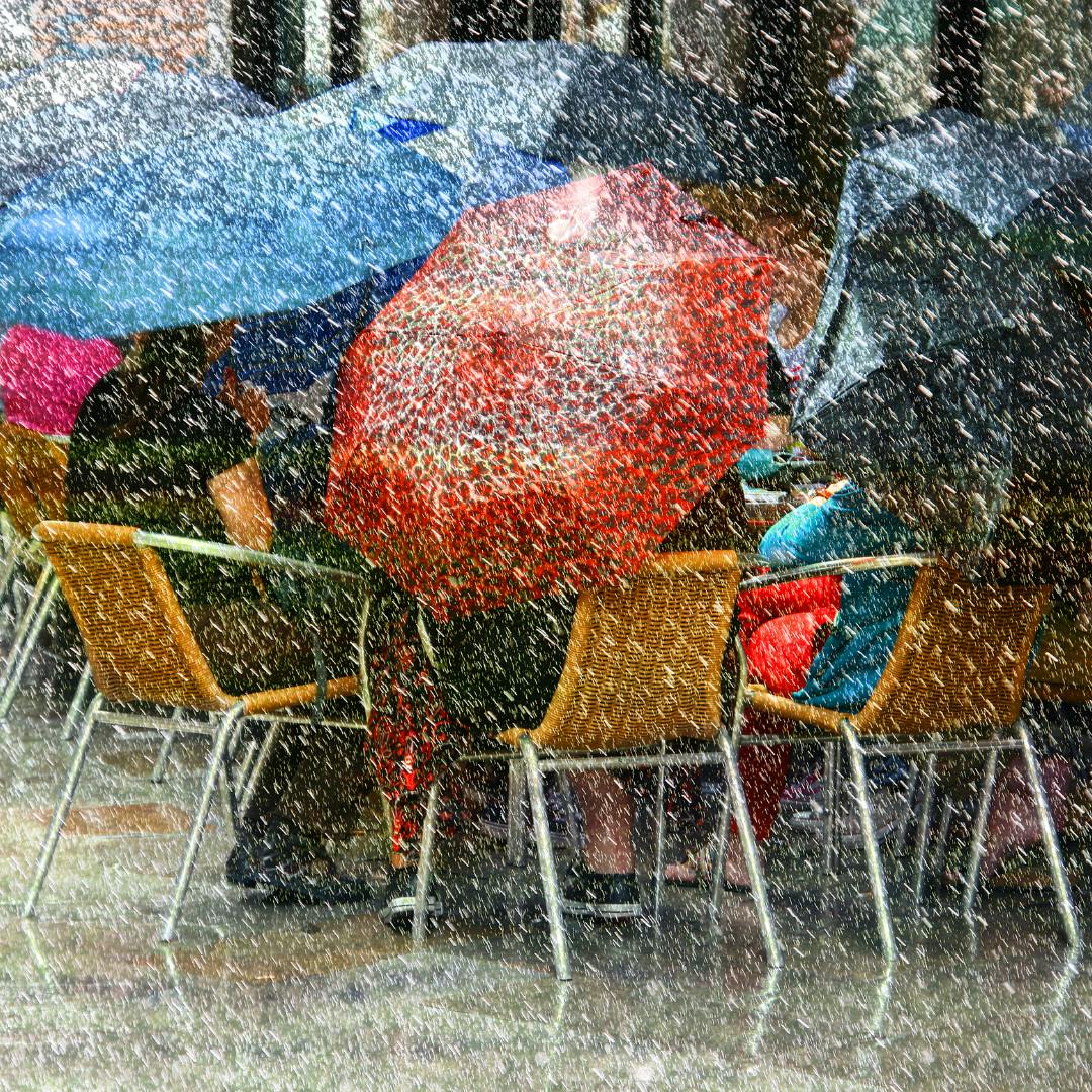 People sat around in outdoor seating beside a café all holding umbrellas in the intense rain