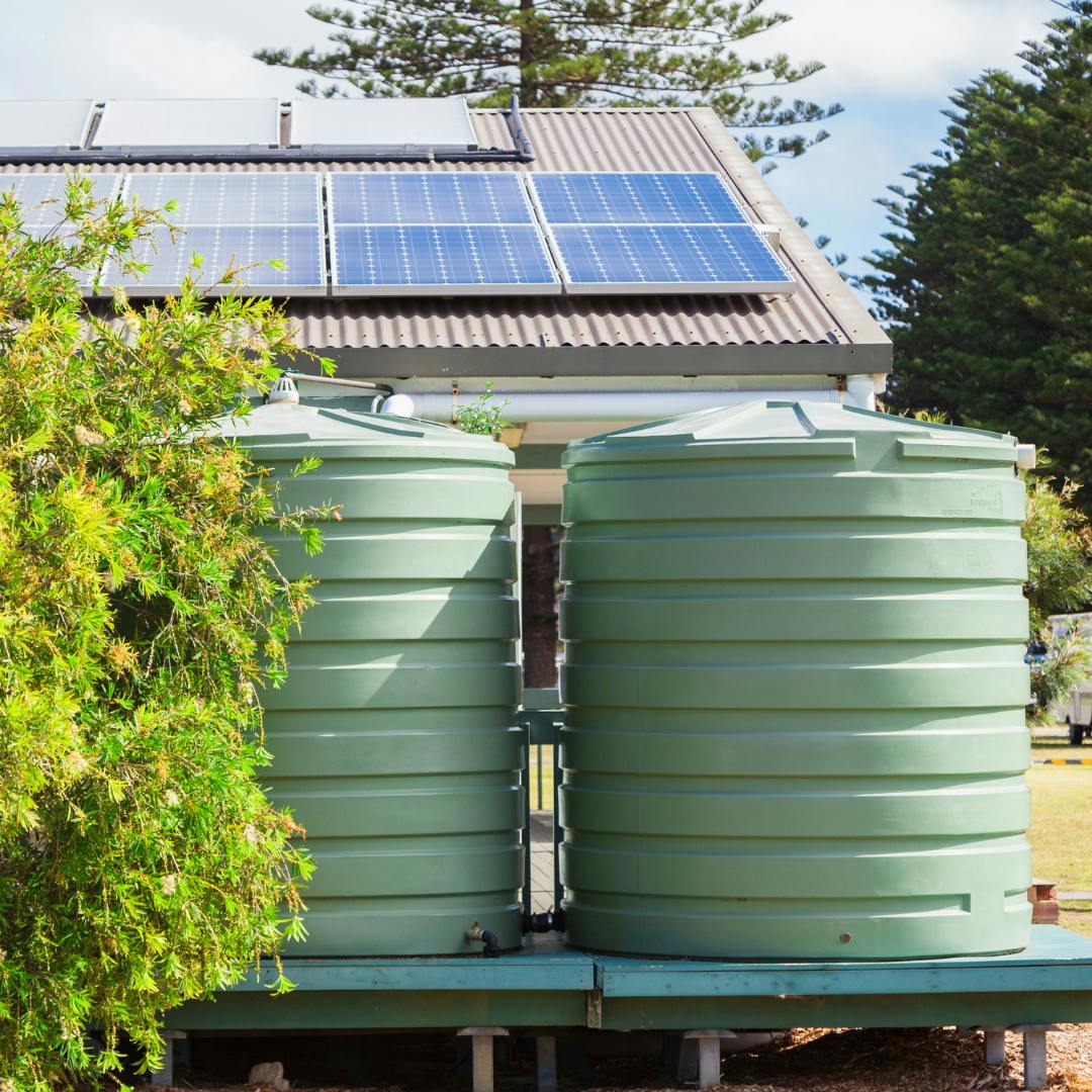 Two large light green rain tanks connected and next to a roof with solar panels on them