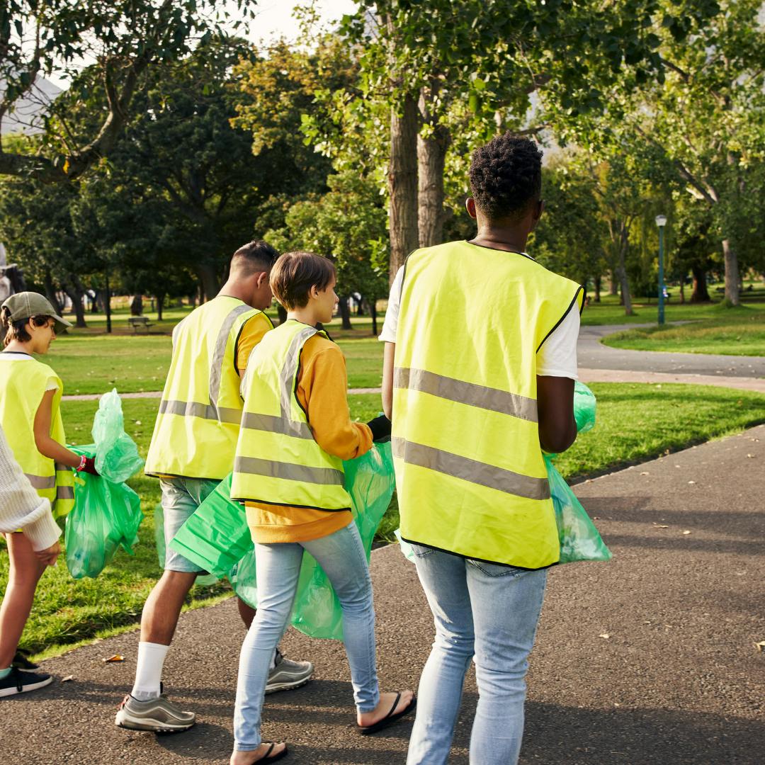 People with high vis jackets and binbags walking through a park