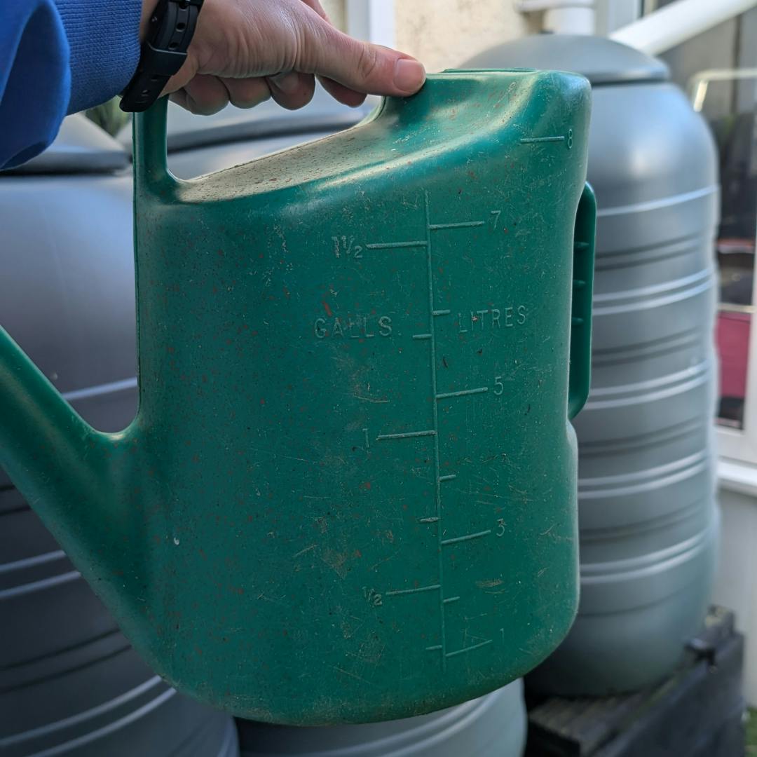 A watering canister being held up in front of water butts