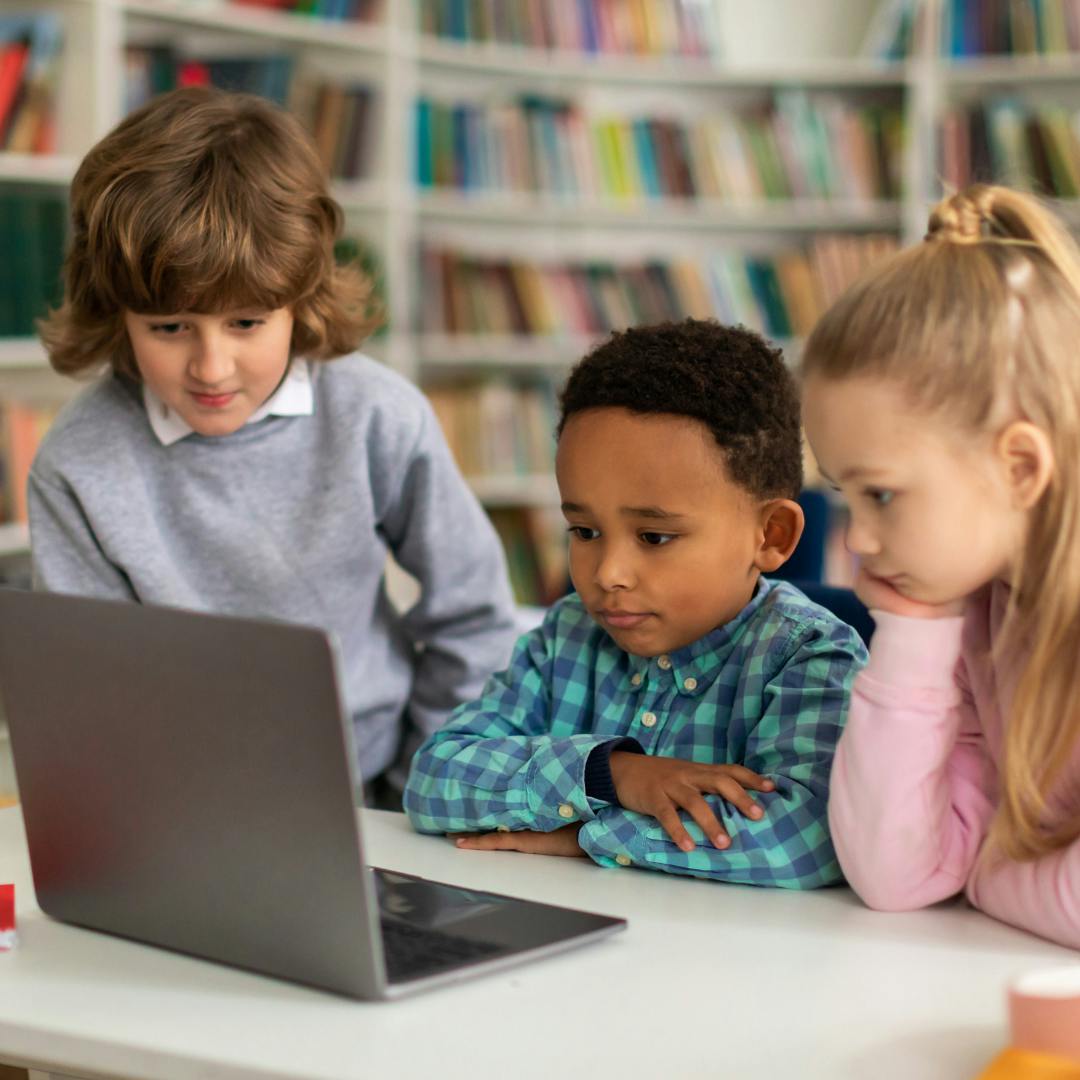 Three young kids gathered around a laptop