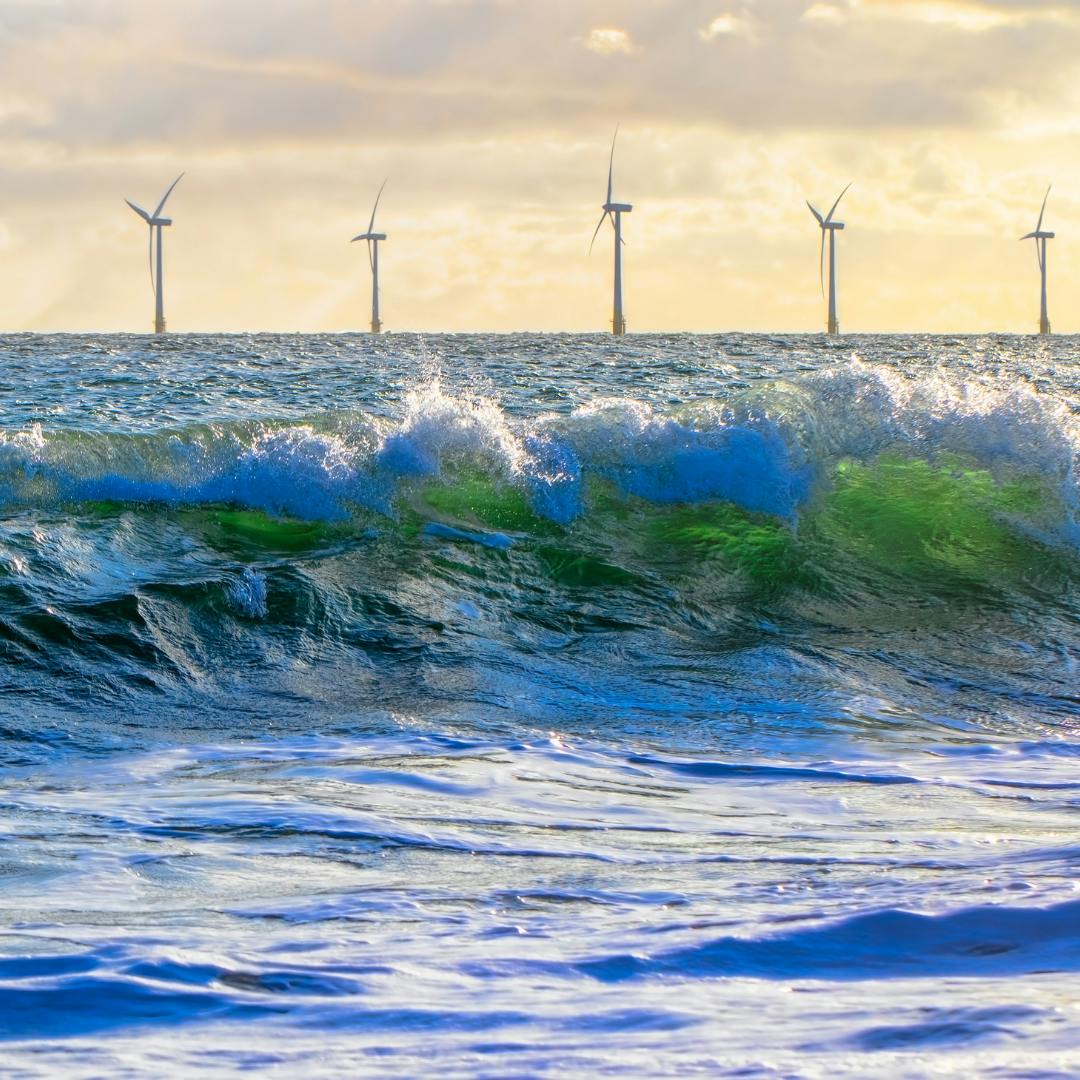 Bluey-Green waves at sea with wind turbines in the background