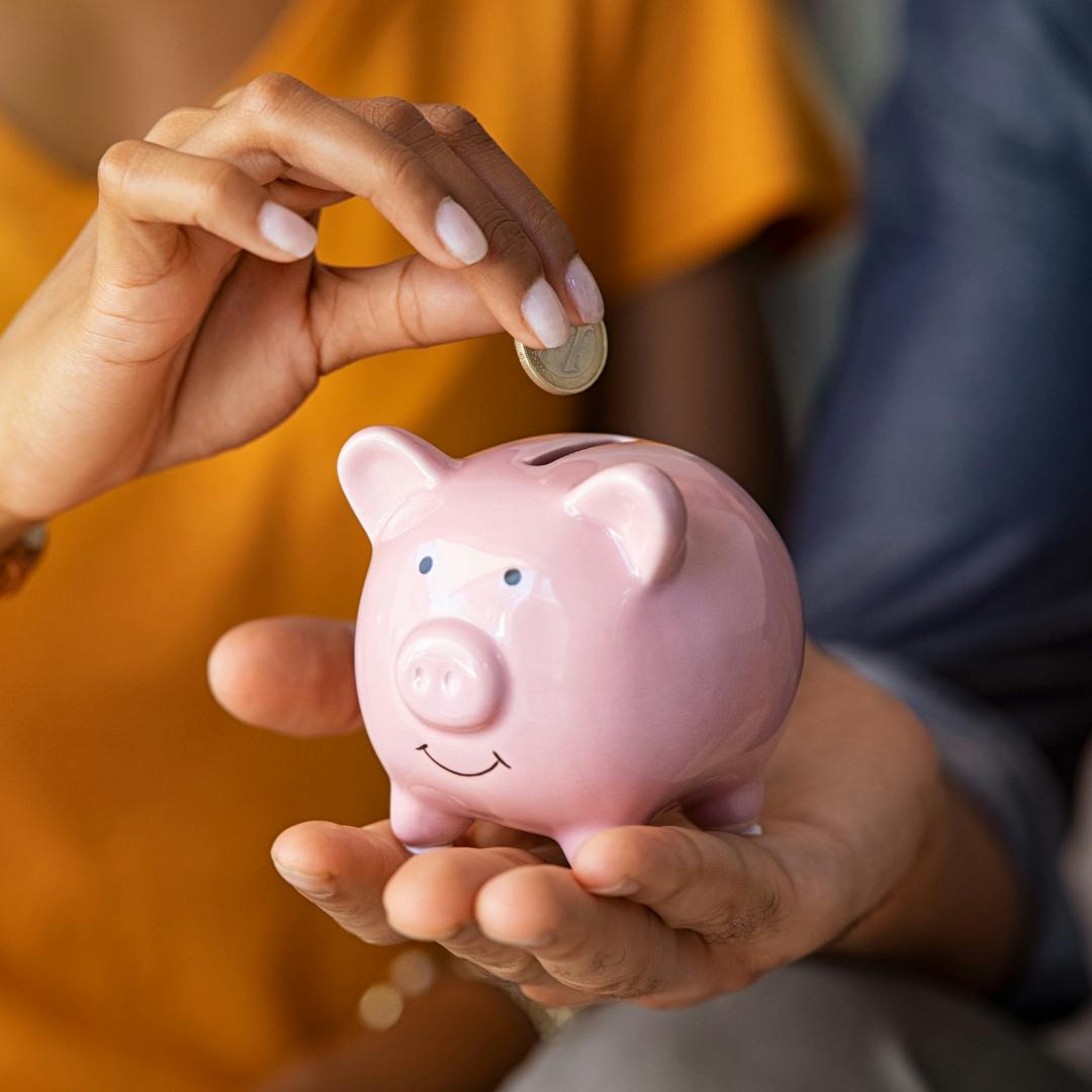 A small pink piggy bank in someone's hand with money being put into it