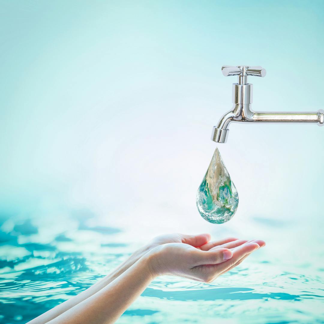 a silver tap with a water drop coming out that reflects the earth above a pair of cupped hands