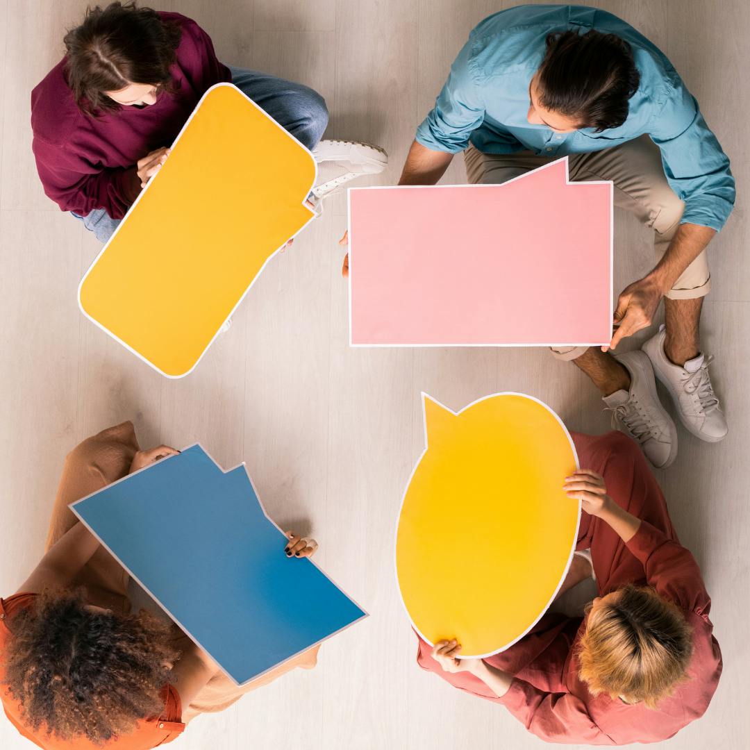 four people sat in a circle holding cards shaped like speech bubbles