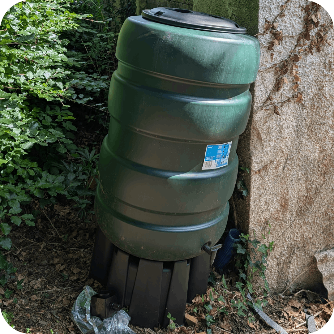 a green water butt against a wall 