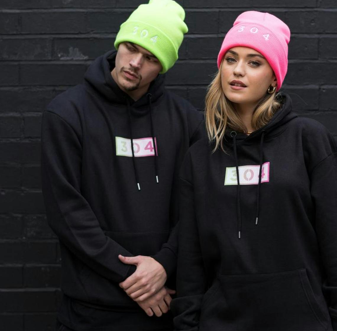 Two models wearing blac 304 branded hoodies and green and pink beanies