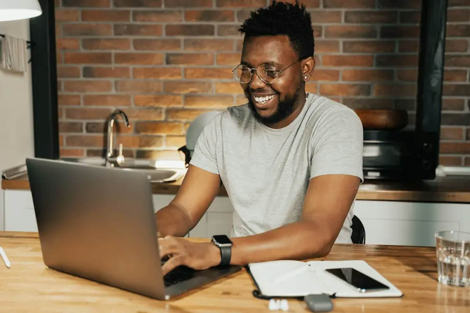 Persona escribiendo en una computadora portátil mientras mira la pantalla y se sienta en el escritorio sonriendo