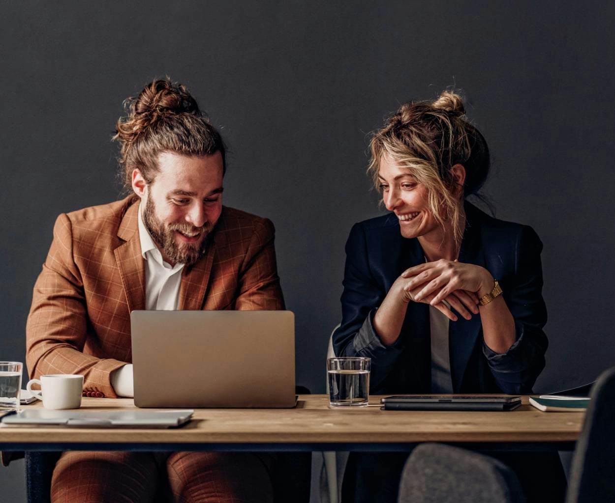 Fundadores masculinos y femeninos sonrientes mirando una computadora portátil y buscando financiación