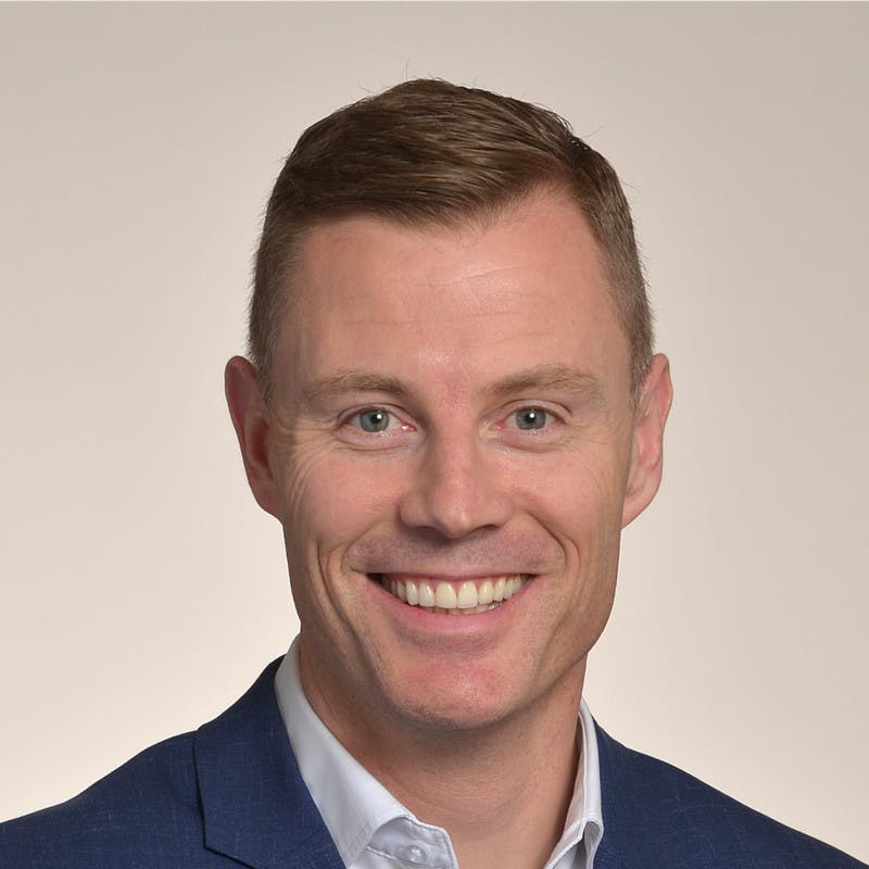 A headshot of a light-skinned man wearing a business suit and smiling.
