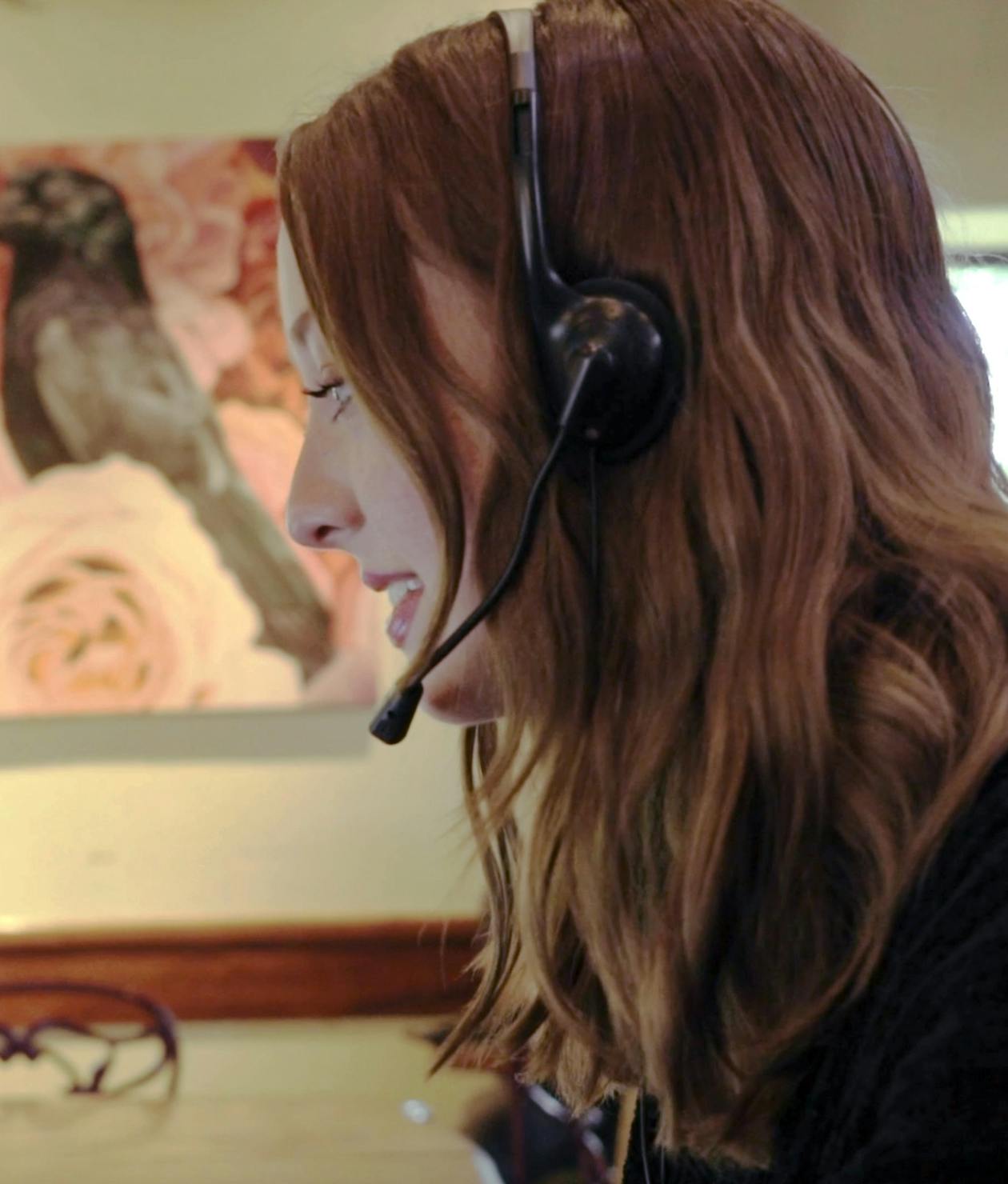 A redheaded woman's side profile as she works wearing a headset.
