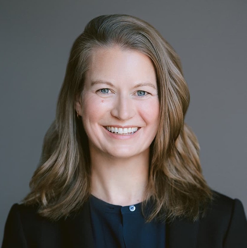 Carla Fowler, performance science expert, wears a dark blazer and top against a gray headshot background.