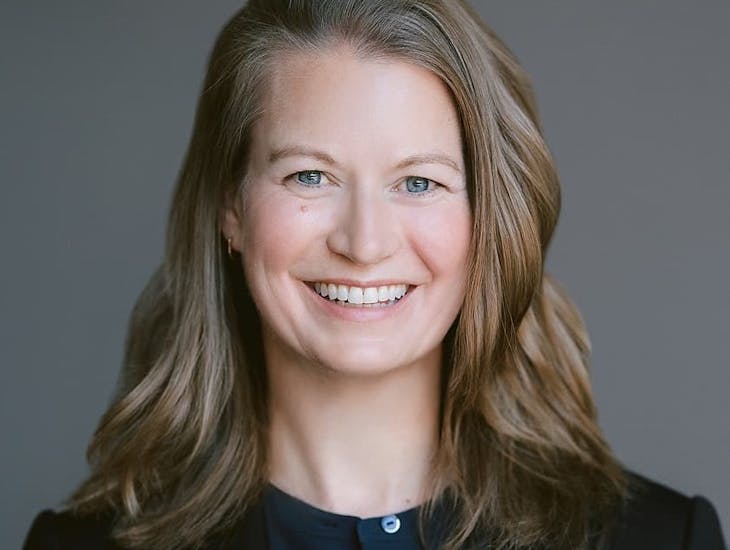 Carla Fowler, performance science expert, wears a dark blazer and top against a gray headshot background.