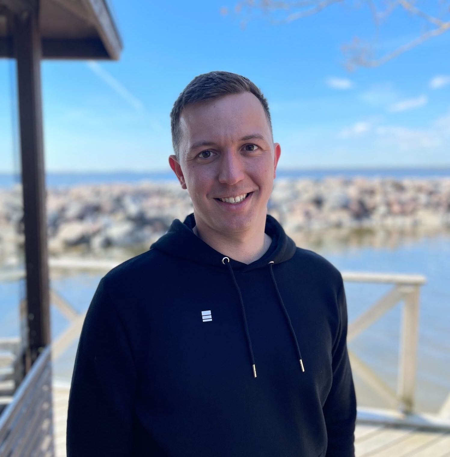 Epicbrief co-founder Anton Dobrzhanskiy smiles while wearing a black hoodie against a scenic coastline.