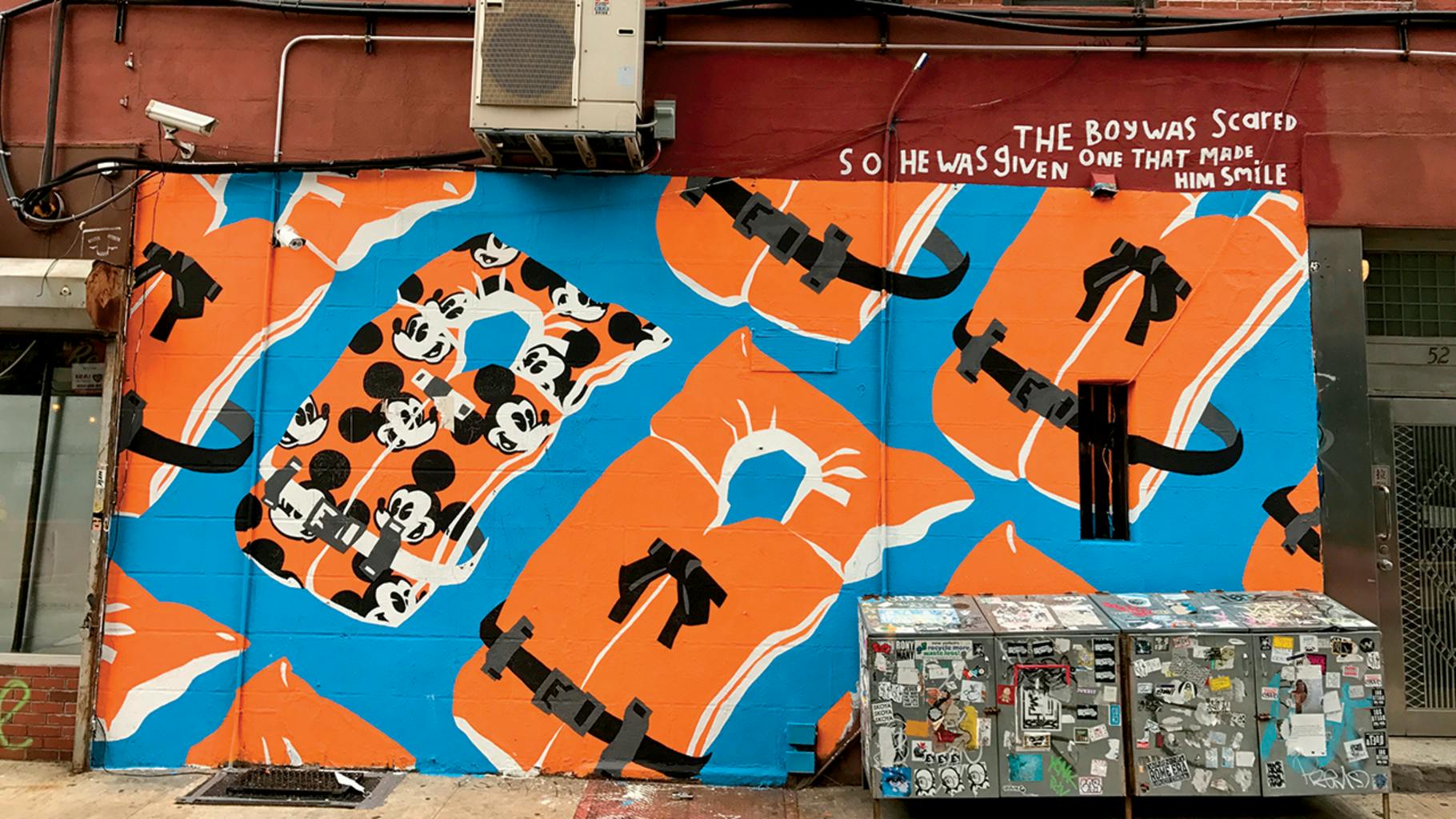 Sink or Swim by artist Adam Lucas was originally done in paint on bleached denim. He was later asked to reproduce the painting as a mural in New York City, as shown here. The work was inspired by an incident in May 2017 off the coast of Libya, when a boat overloaded with some 200 migrants capsized while attempting to reach Europe. Though many were rescued, several dozen died -- reportedly, most of them were very young children. The piece is in response to one specific disaster, but it can be applied to any number of refugee crises. The artist asks us to imagine being part of a family living in an environment so dire that the best hope lies across the uncertain sea. The Mickey Mouse life vest, representing joy and innocence, references an actual child making the journey as well as blameless youth being forced into a situation of such severity. Loss of childhood at best, loss of life at worst.