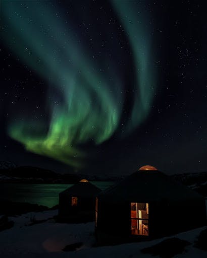 Vakkert grønt nordlys over en mørklagt hytte