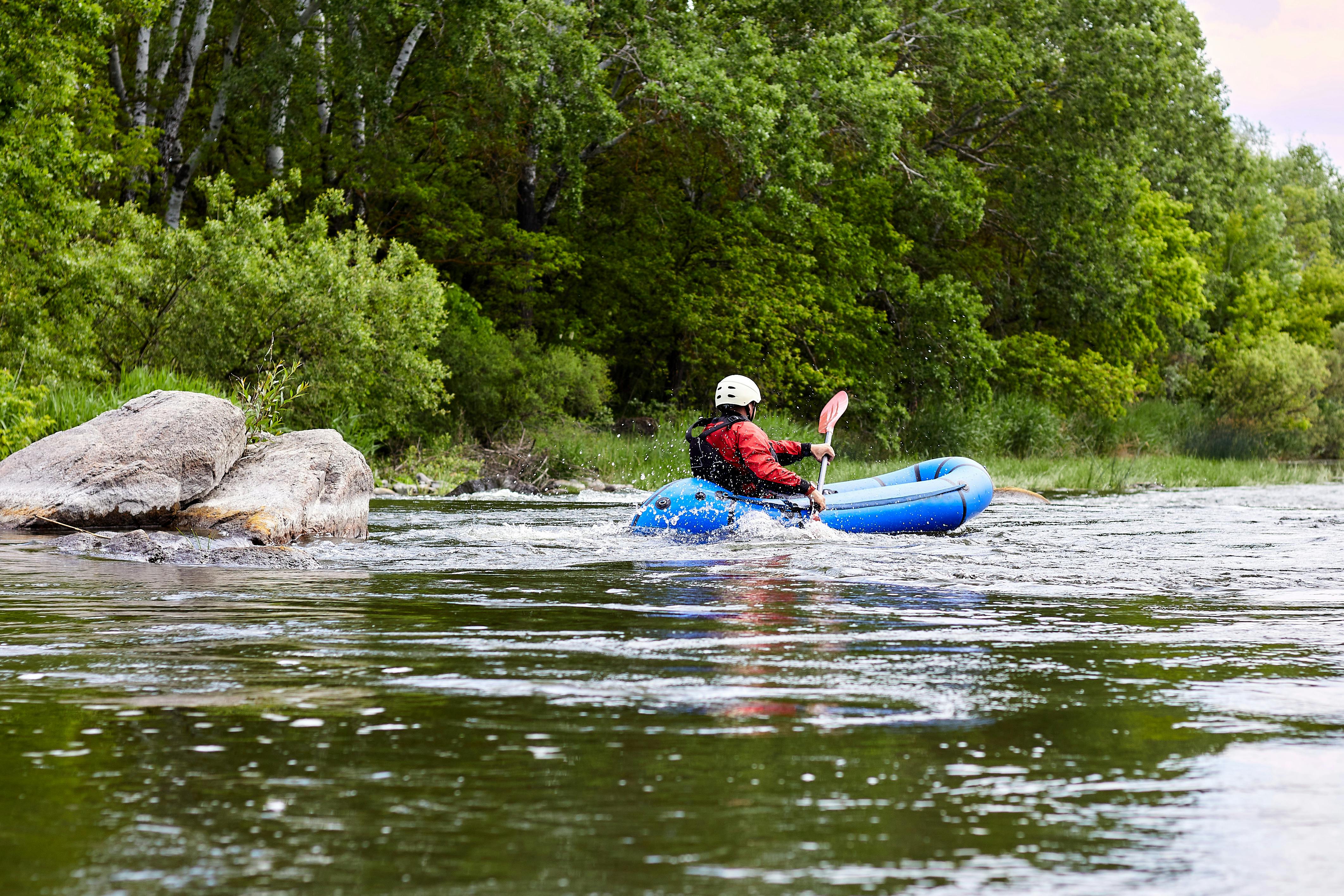 Man paddling an inflatable blue packraft on a river in early spring spring
