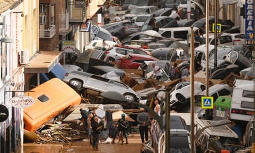 Fotografia de uma rua da Espanha durante as chuvas intensas de outubro de 2024. Nela, são vistos vários carros amontoados, que foram arrastados pela água, que ocupam toda a rua.